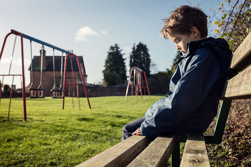 Sad little boy sitting alone on a bench at the park