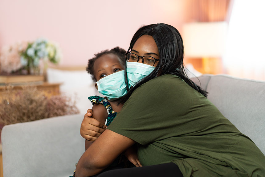 African American woman hugging her daughter, both wearing masks