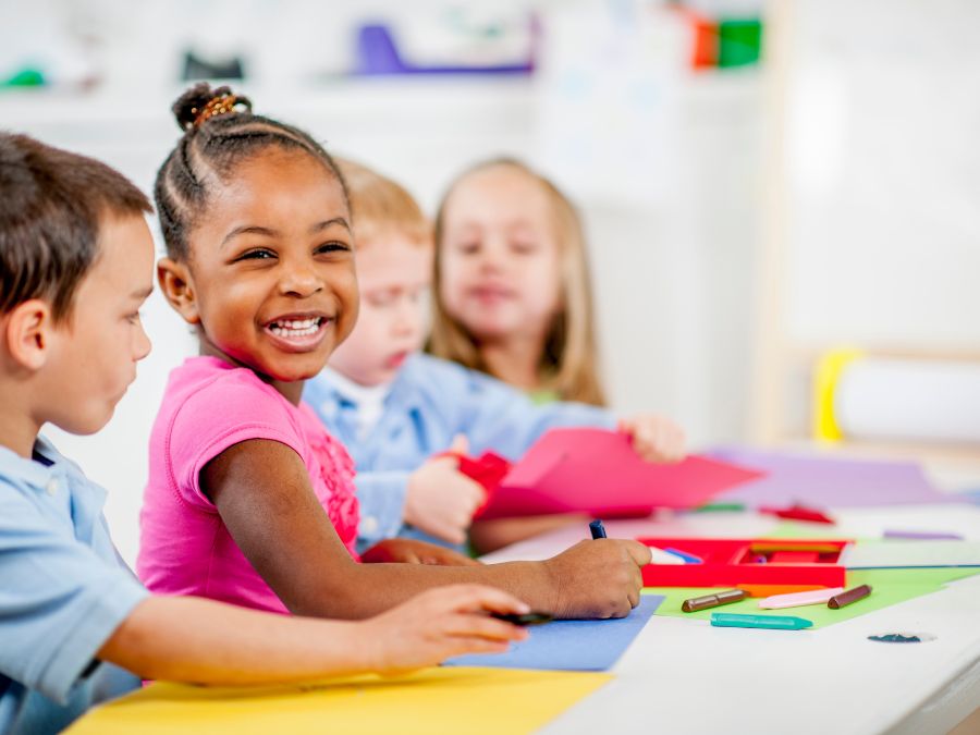 Children coloring at school with young girl smiling.