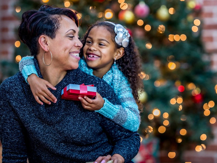 Mother carrying young daughter on her back while daughter holds a present.