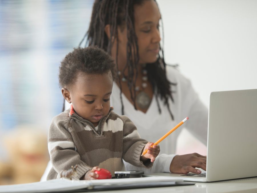 Mother working on laptop and small child coloring with pencil.