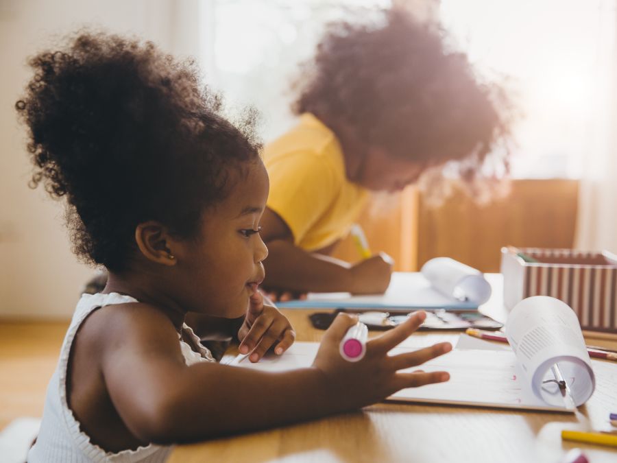 Young children sitting down and coloring at table.